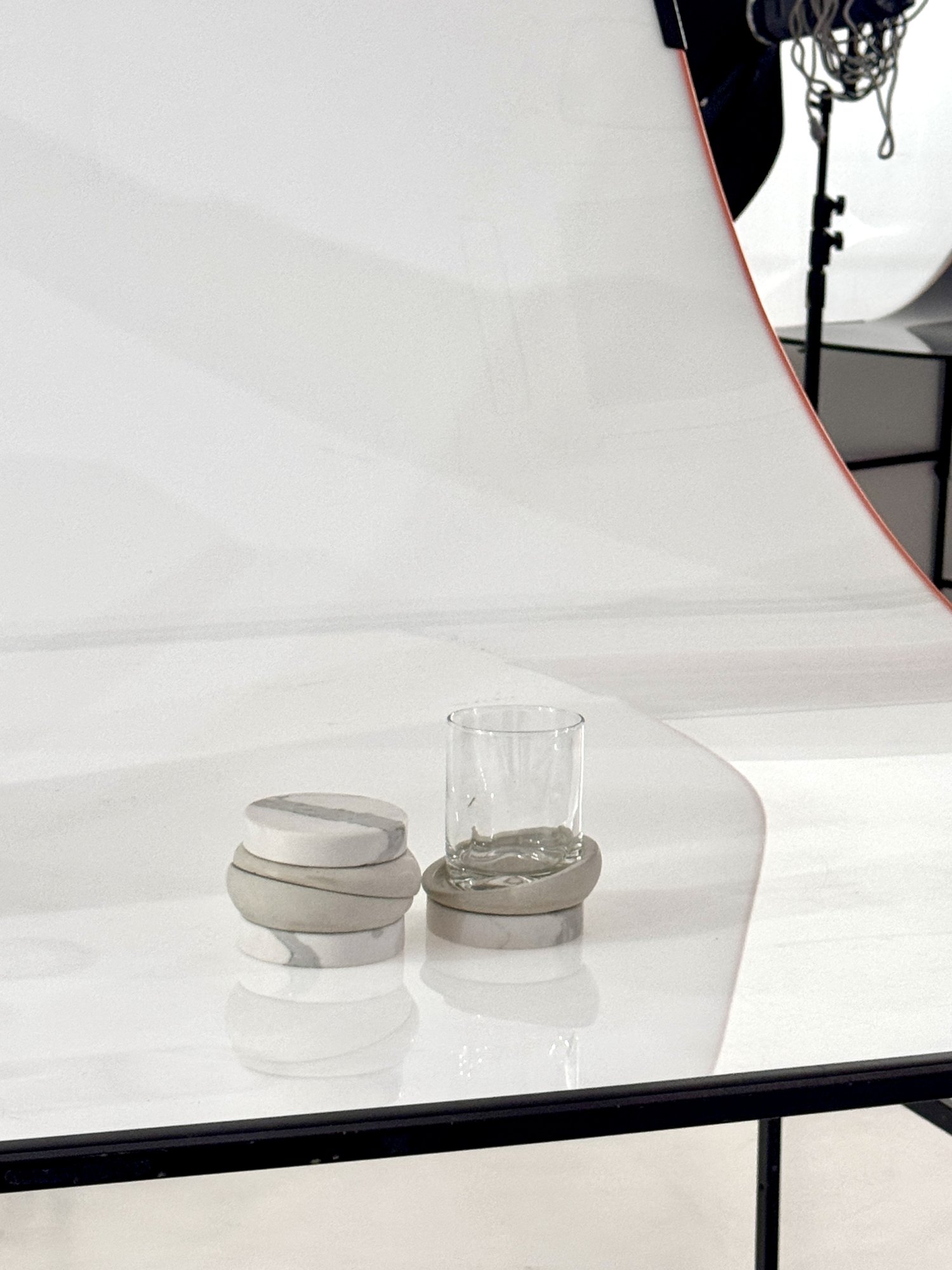 Pieza de mármol y concreto junto a un vaso de vidrio sobre un fondo blanco de estudio
