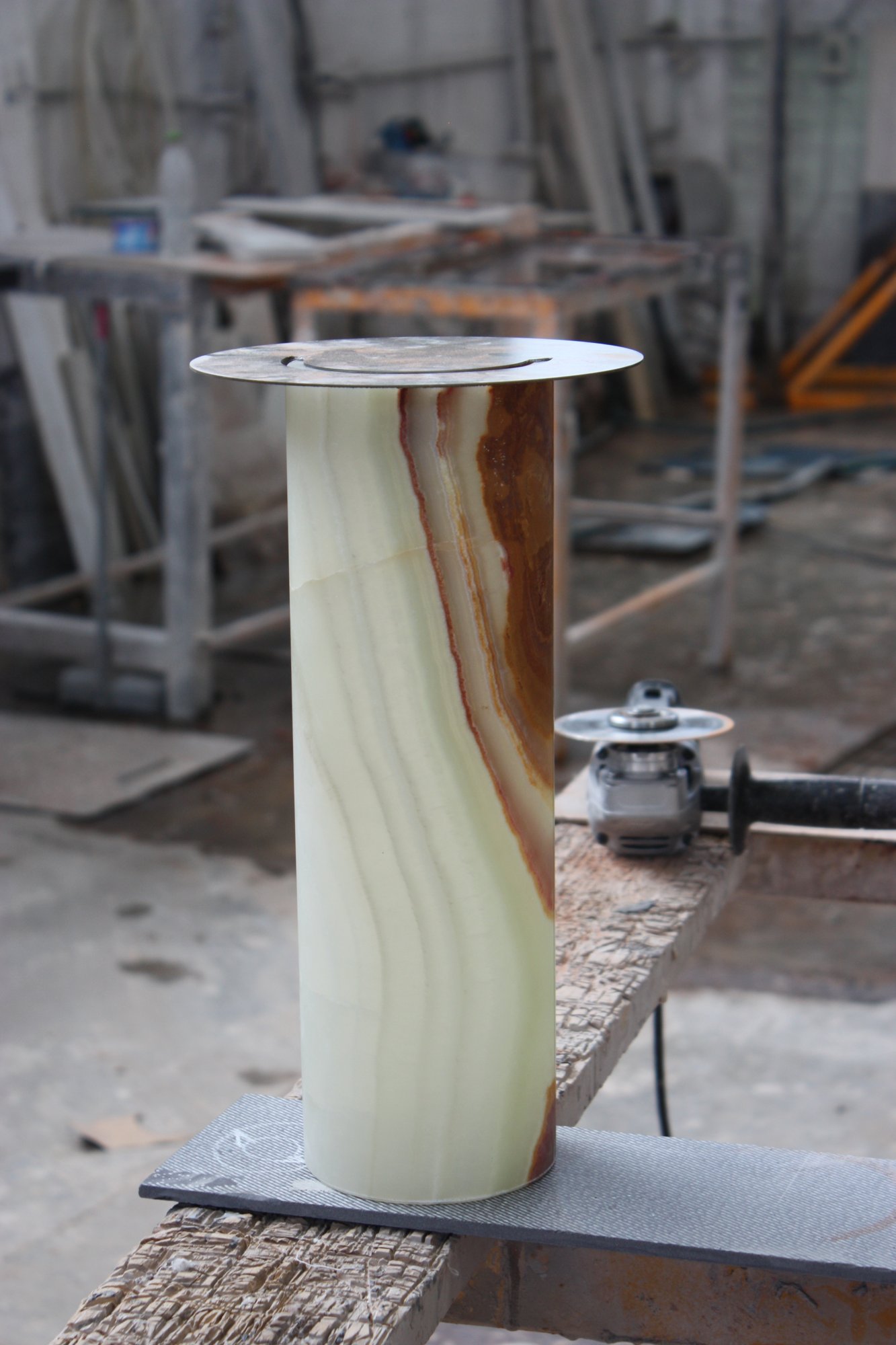 Cilindro de ónix verde y ámbar con un disco metálico, sobre una tabla en el taller